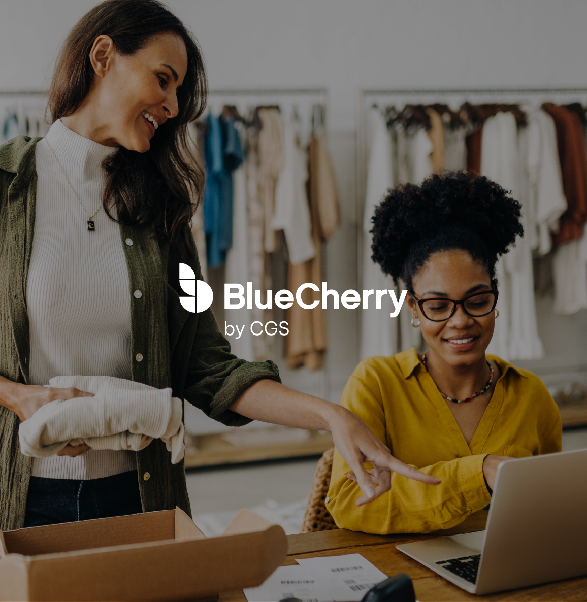 Two clothing manufacturing professionals working at a desk, clothes racks are behind them, and the BlueCherry logo is overlayed on top of them