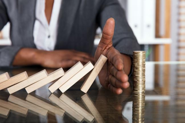 How to Reduce Risks with Outsourcing Businessperson hand blocks domino effect on tower of coins