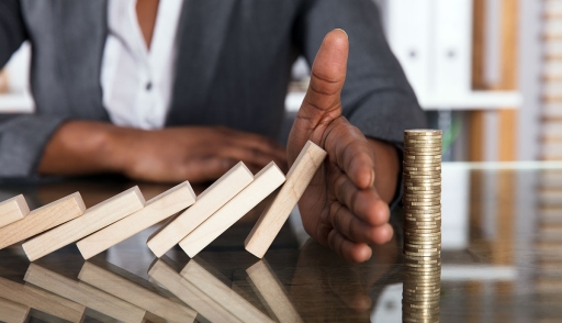 Businessperson hand blocks domino effect on tower of coins